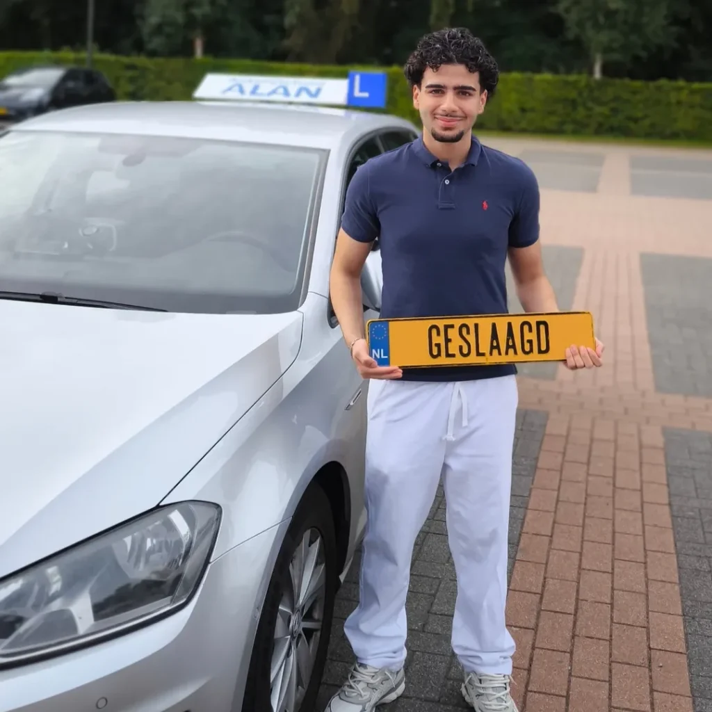 Geslaagde rijexamen kandidaat Aryan toont trots zijn GESLAAGD kenteken bij witte auto van Autorijschool ALAN Geslaagde rijexamen kandidaat Aryan toont trots zijn GESLAAGD kenteken bij witte auto van Autorijschool ALAN