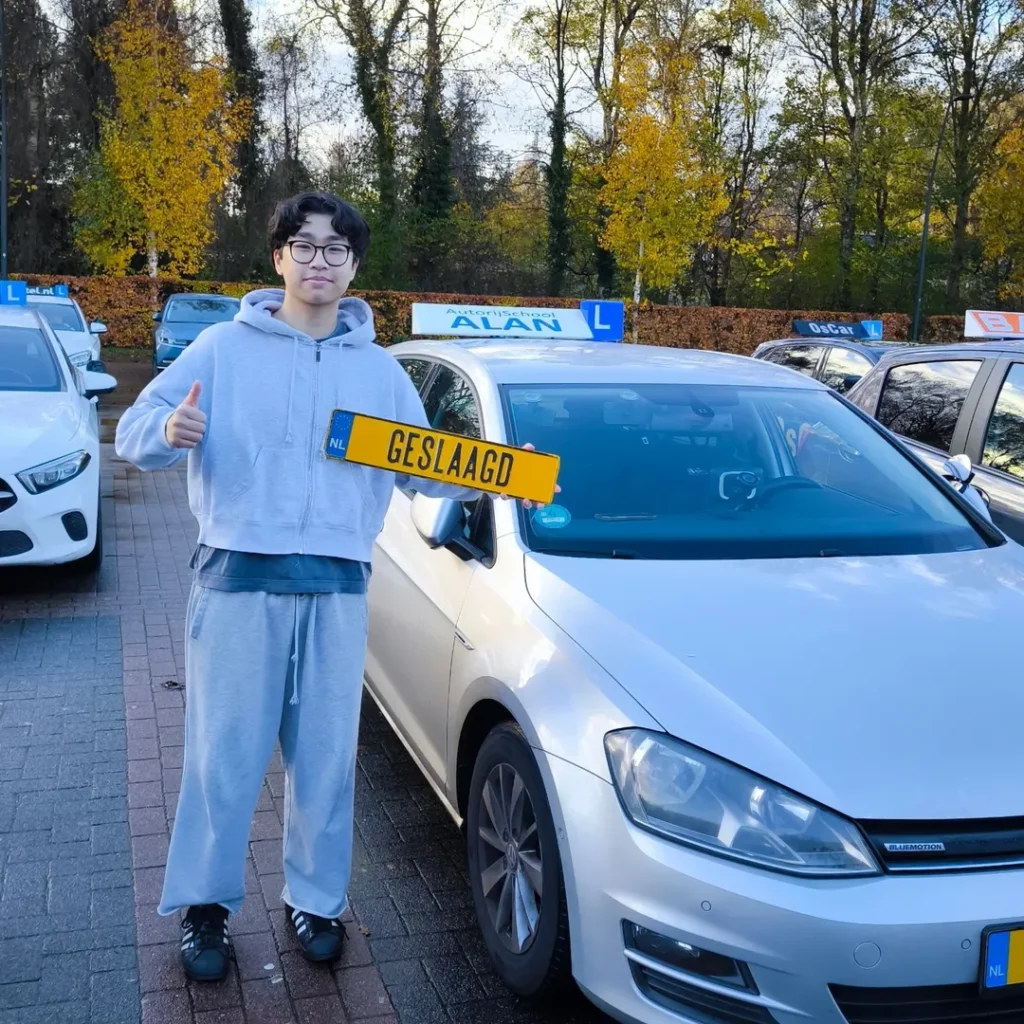 Geslaagde rijleerling Bao toont rijbewijs na succesvol rijexamen bij Autorijschool ALAN met witte lesauto Geslaagde rijleerling Bao toont rijbewijs na succesvol rijexamen bij Autorijschool ALAN met witte lesauto