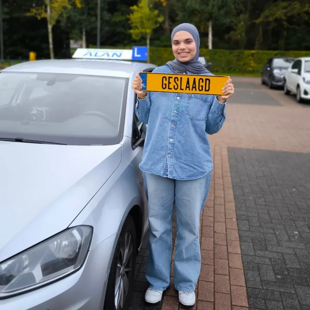Jonge vrouw met hoofddoek houdt gele 'GESLAAGD' plaat vast na het behalen van rijexamen bij Autorijschool ALAN Jonge vrouw met hoofddoek houdt gele 'GESLAAGD' plaat vast na het behalen van rijexamen bij Autorijschool ALAN